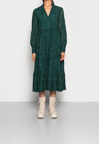 Grön spetsklänning med långa ärmar, v-ringning, lager-på-lager kjol och utskurna mönster. Matchad med ljusbeiga snörade ankelstövlar.