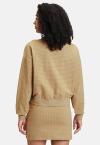 Pullover beige a quadri con maniche lunghe e orlo a costine; abbinato a una gonna a quadri coordinata, entrambi realizzati in un tessuto morbido e testurizzato.