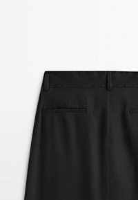 Vue arrière d’un pantalon noir avec passants de ceinture et deux poches arrière horizontales sur fond blanc.