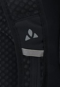 Tessuto nero con un motivo testurizzato, con un logo grigio e una striscia riflettente lungo la cucitura. Materiale liscio e resistente.