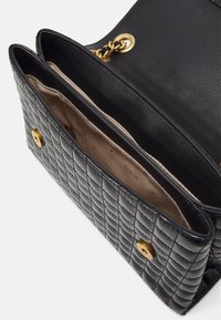 Sac à main en cuir matelassé noir avec un bouton en matériel doré et des détails en chaîne. L'intérieur est doté d'une doublure en tissu beige et d'un espace de rangement suffisant.