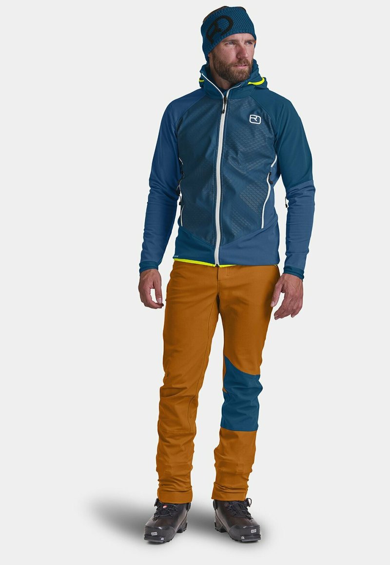 Blue and teal hooded jacket with textured front, paired with brown pants featuring a teal patch. Both garments are made from stretchy fabric.