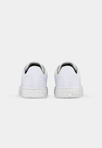 Une paire de baskets blanches basses vues de l'arrière avec le texte en relief "TOMMY JEANS" sur les semelles intermédiaires.