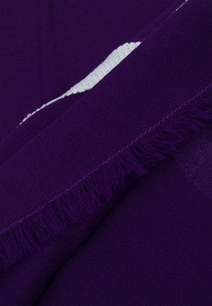 Tissu violet plié avec un bord à franges visible et une petite section de matière tricotée blanche contrastante en dessous.
