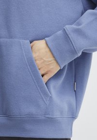 Felpa blu con tasca a marsupio, polsini e vita a coste. Tessuto morbido, branding minimo sul lato.