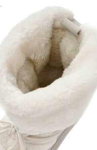 Bota forrada de felpa blanca con una textura suave, cuello redondeado y cordones beige. Cuenta con una pequeña tirador de tela en la parte superior.
