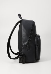 Zaino nero con una finitura liscia, zip superiore e tasca laterale con zip. Dotato di spallacci regolabili. Design minimalista.