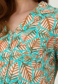 Korte mouwen shirt met een turquoise basis, met een levendig bladerenpatroon in oranje en bruin, voorzien van knoopdetails en een klassieke kraag.