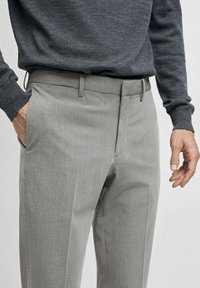 Pantaloni grigi in tessuto strutturato, taglio slim, con tasche laterali e cintura liscia, abbinati a un top a maniche lunghe grigio scuro.