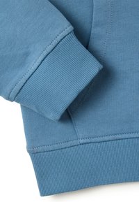 Manga de sudadera azul con puño acanalado doblado sobre la cintura acanalada contra un fondo blanco.