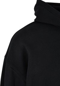 Felpa con cappuccio nera, caratterizzata da un tessuto morbido e texture, vestibilità leggermente oversize e dettagli di cucitura minimal lungo le cuciture.
