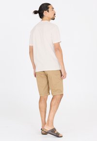 Beige bomulls t-shirt, knähöga khakishorts och bruna sandaler med dubbelbuckle. Modell sedd bakifrån, håret uppsatt i en knut.