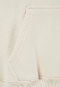 Nahaufnahme eines beigen Sweatshirts, die eine Fronttasche, einen gerippten Saum und eine glatte Textur mit subtilen Nähten zeigt.