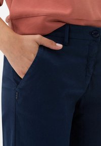 Námořnické modré kalhoty vyrobené z lehkého materiálu, s předními kapsami, zapínáním na knoflík a rovnými nohavicemi. Hladký povrch s minimálním zdobením.