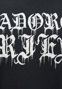 Λευκός γοτθικού στυλ κείμενο με σταγόνες σε μαύρο ύφασμα που δείχνει μερικές λέξεις "AY NOR" και "AKY".