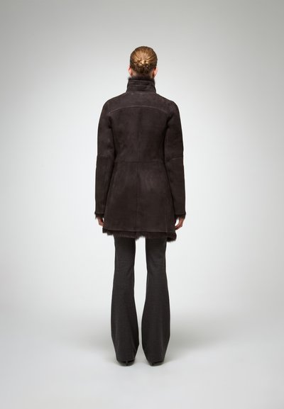 Palton din suede maro închis cu guler înalt și margine din blană moale, purtat cu pantaloni sobri, bine croiți. Design elegant și ajustat.