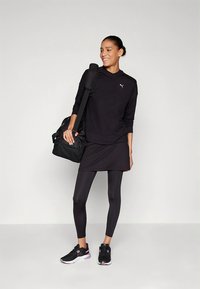 Black athletic outfit featuring a long-sleeve hoodie, layered tunic, and leggings. Worn with black sneakers and a black gym bag.