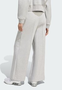 Pantalones sudadera de gran tamaño en gris claro con piernas anchas y costuras laterales, combinados con zapatillas deportivas blancas. Textura suave con un ajuste relajado.