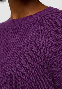 Fialový pletený svetr s texturovaným vzorem a žebrovaným detailem na límci a ramenou, zdůrazňující měkkost a teplo.