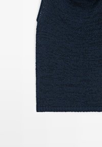Dunkel marineblaues, gestricktes ärmelloses Oberteil mit einfachem Muster, flach auf einem weißen Hintergrund liegend.