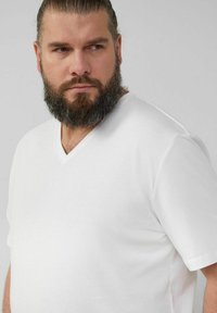 Weißes Baumwoll-V-Ausschnitt-T-Shirt mit kurzen Ärmeln, ausgestattet mit einem dezenten Markenlogo auf der Brust und einer lockeren Passform. Glatte Textur.