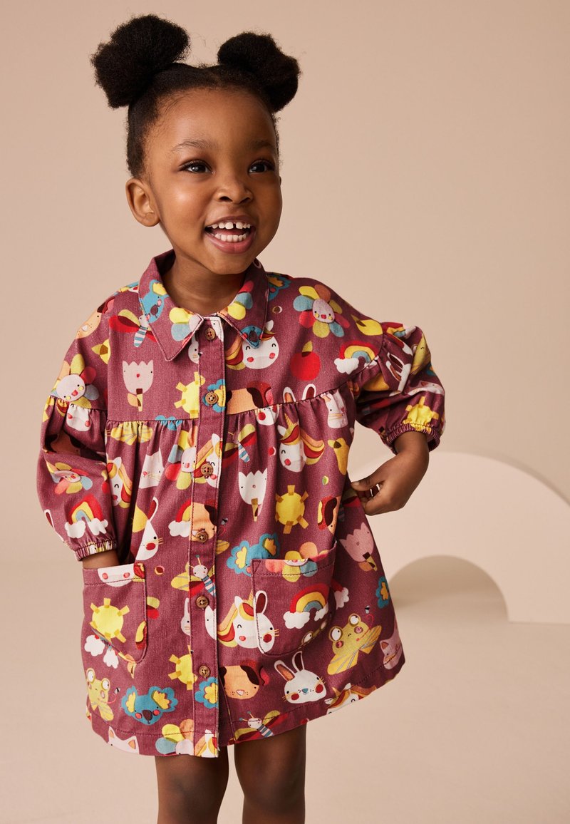 Maroon dress with colorful, cartoon animal and flower patterns, button-down front, and pockets. Long sleeves with elastic cuffs.