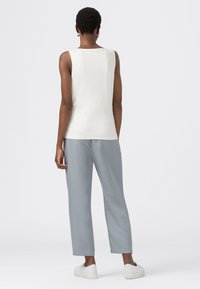 Vit ärmlös topp med rund halsringning, ihopparad med ljusgrå, löst sittande byxor. Enkelt mönster, mjuk textur och neutrala färger.