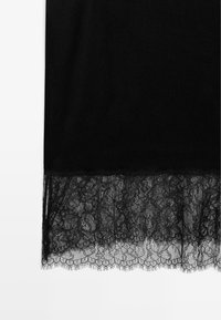 Tessuto nero con un orlo in pizzo dettagliato. Il pizzo presenta motivi floreali con un bordo a onde, in contrasto con il materiale liscio soprastante.