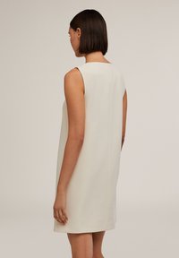 Rochie fără mâneci, de lungime până la genunchi, dintr-un material alb-crem. Siluetă simplă, dreaptă, cu un decolteu rotund și un spate neted, fără embellismente.