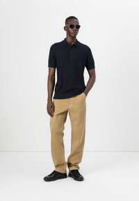 Polo shirt bleumarin cu mânecă scurtă; pantaloni largi de nuanță bej deschis; adidași negri; ochelari de soare negri; textură de țesătură netedă, potrivire casuală.