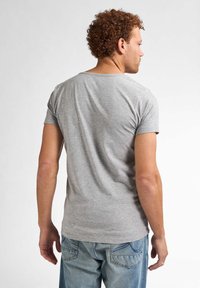 Tricou gri cu mânecă scurtă, cu guler rotund, confecționat dintr-un material de bumbac neted; purtat cu blugi de culoare albastru deschis.