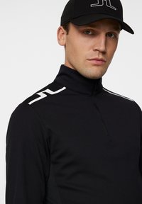 Svart zip-up topp med hög krage, med vita accentlinjer på axlarna. Tight passform, textil med struktur, lämplig för sportkläder.