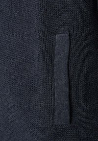 Zbliżenie na ciemnoniebieską dzianinę z pionową kieszenią wbudowaną w teksturę.