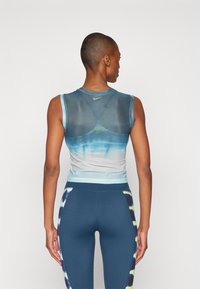 Lengvas, be rankovių debesis mėlynos ir žalios gradientinės spalvos, su permatomu dizainu ir Nike logotipu; suderinti su tamsiai mėlynomis leggingais su raštuotais akcentais.