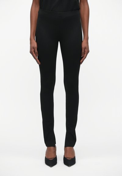 Black leggings made of stretchy, smooth fabric. Tailored fit with a slim shape and subtle side slits at the hem. Paired with black heels.