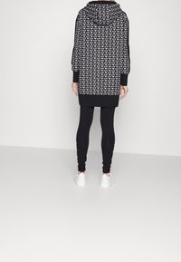 Czarna sukienka z kapturem i długimi rękawami z białym wzorem logo. Noszona z czarnymi legginsami i białymi sneakersami. Minimalistyczny design.