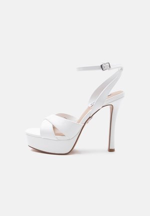 Valged kõrge kontsaga platvormkingad, millel on pahkluu ümber rihm ja pandlaga kinnis, avatud varvas ning esiküljel risti üle käivad rihmad.