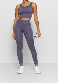 Top corto a coste viola e leggings a vita alta coordinati, completati da sneaker bianche e una bottiglia d'acqua. Texture morbida, design aderente.