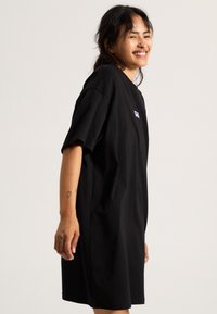 Robe t-shirt en coton noir à manches courtes, coupe décontractée et petit logo blanc sur la poitrine. Texture lisse et longueur au genou.