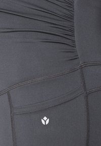 Sorte atletikleggings med samlet tekstur ved taljen, med en lille hvid logo og flatlock-sømme.