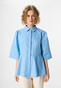 Lichtblauwe blouse met kraag, driekwart pofmouwen en een peplum taille ontwerp, gemaakt van een gladde stof.
