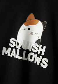 Un tejido negro presenta un gato de dibujo animado con un patrón marrón y blanco. El texto debajo dice "SQUISH MALLOWS" en una fuente plateada en negrita.