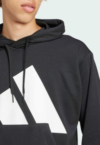 Black hoodie made of soft fabric; features a large white geometric design. Includes a front pocket and a drawstring hood.