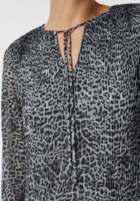 Schwarz- und grau gemusterte Bluse mit plissierter Textur, V-Ausschnitt und Bindung am Hals. Transparente Ärmel.