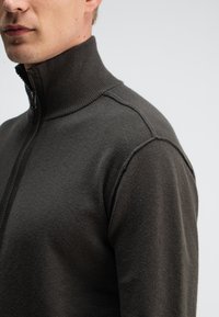 Dunkelgrauer, leichter Pullover mit einem hohen gerippten Kragen, halber Reißverschluss und kurzen Ärmeln. Verfügt über eine glatte Textur und eine taillierte Passform.