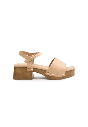 Sandalia de cuero beige con puntera abierta, correa en el tobillo y tacón bloque. Presenta acentos de tachuelas en tono dorado y una plantilla texturizada.