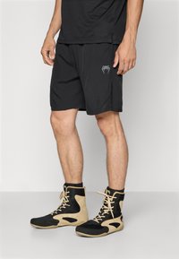 Shorts de sport noirs avec un détail de logo subtil, associés à des baskets montantes présentant un design en maille et des accents beiges, mettant en valeur un contraste de textures.