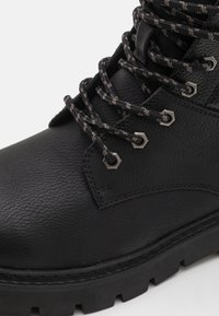 Stivale in pelle nera con superficie texturizzata, occhielli metallici e lacci neri e grigi a motivo. Dotato di una suola in gomma spessa.