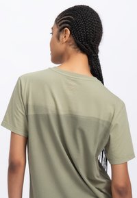 T-shirt verde oliva a maniche corte con una consistenza morbida, caratterizzata da un delicato design sfumato e un piccolo logo vicino al collo sul retro.