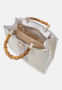 Sac à main blanc et beige avec des anses style bambou, dessus ouvert montrant des compartiments intérieurs avec fermeture éclair et une doublure au logo Guess.
